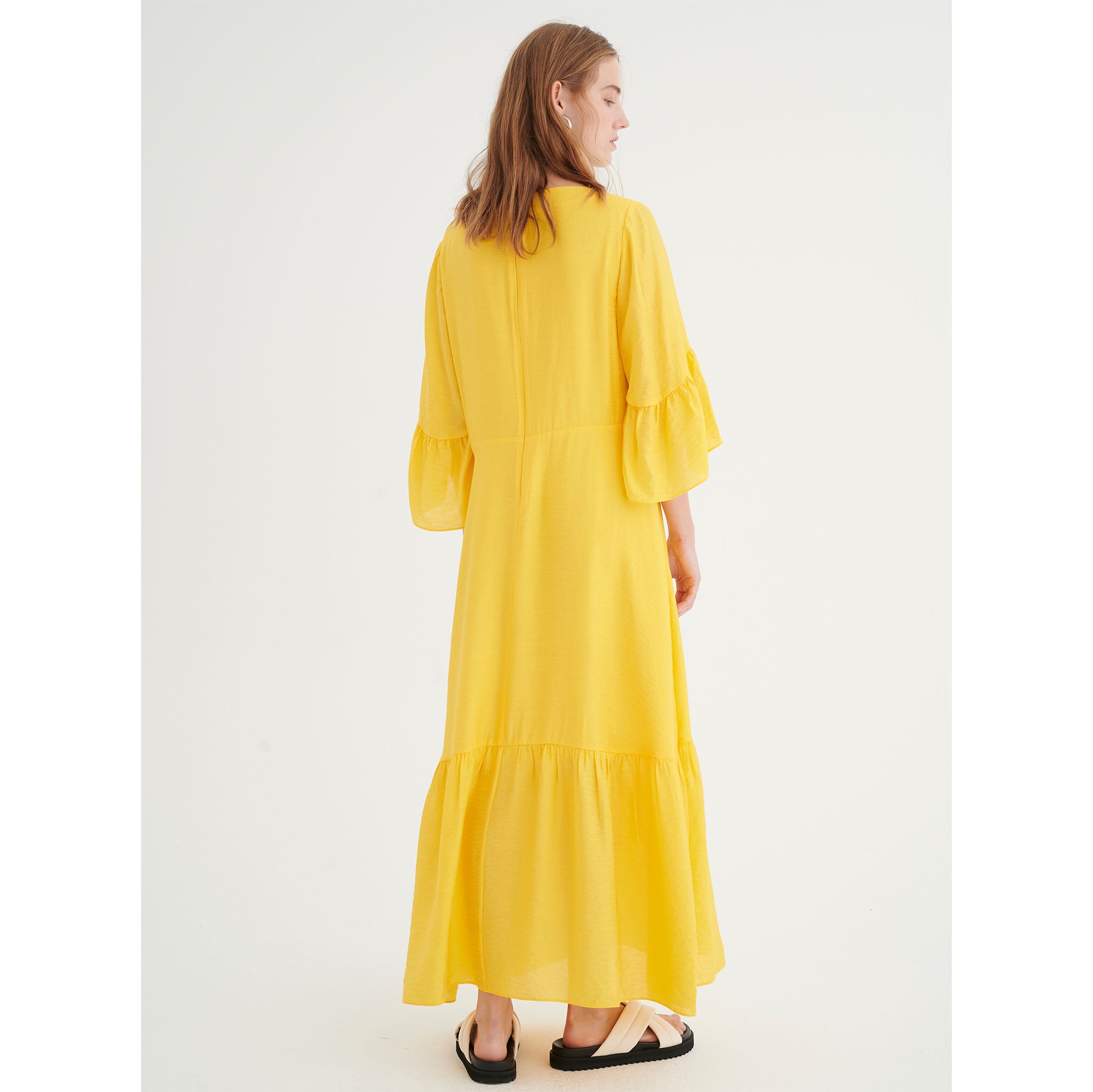 In Wear, kirkkaan keltainen, pitkä mekko. Frillat hihoissa ja helmassa. Takakuva mallin päällä.