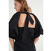 In Wearin musta, näyttävä mekko. Suuret puhvihihat ja avoin selkä. Lähikuva mallin päällä.