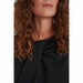 In Wear, naisten musta hihaton pusero. Edessä epäsymmetrinen laskos ja poimutusta. Lähikuva mallin päällä.